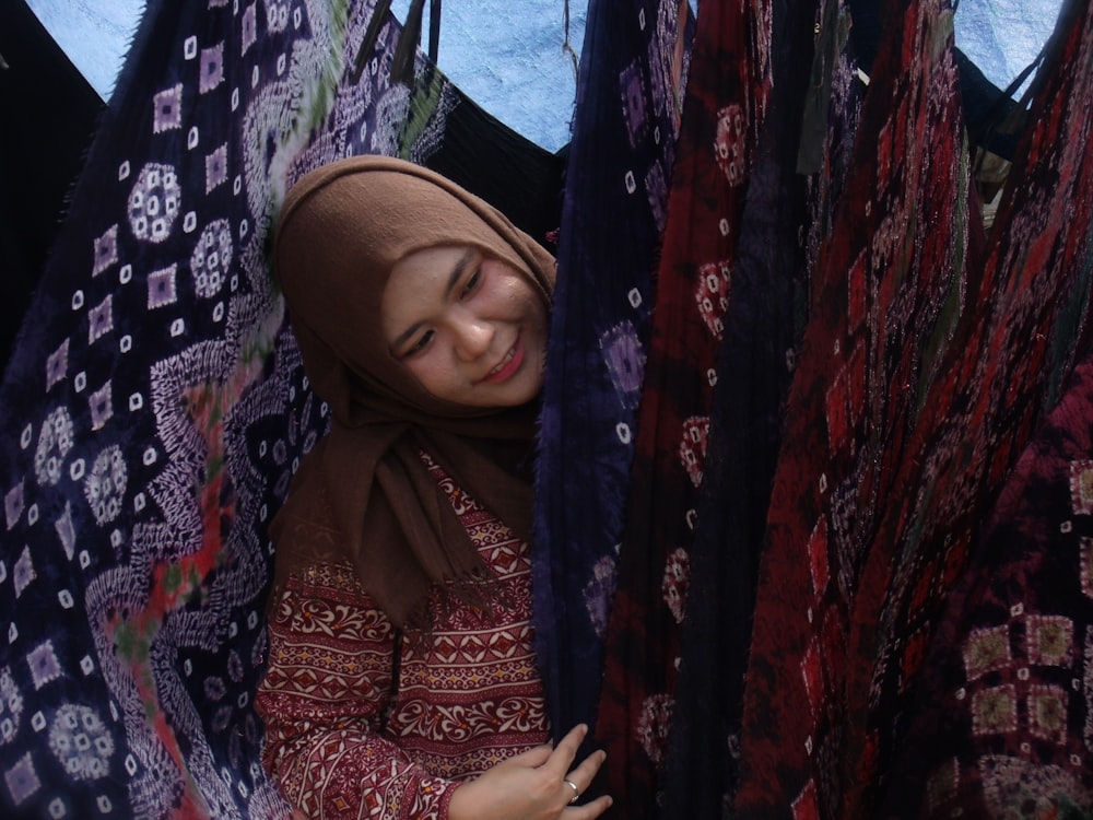 Frau mit braunem Hijab, die sich vor geblümten Textilien versteckt