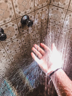 Hands fitting a shower set in a tiled bathroom wall.