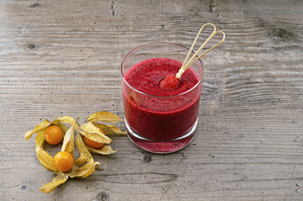 red liquid on glass cup beside fruits on gray wooden surface