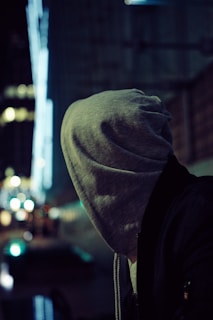 Lifestyle shot of a young adult wearing a charcoal gray Monowear hoodie against an urban Tokyo backdrop at dusk.
