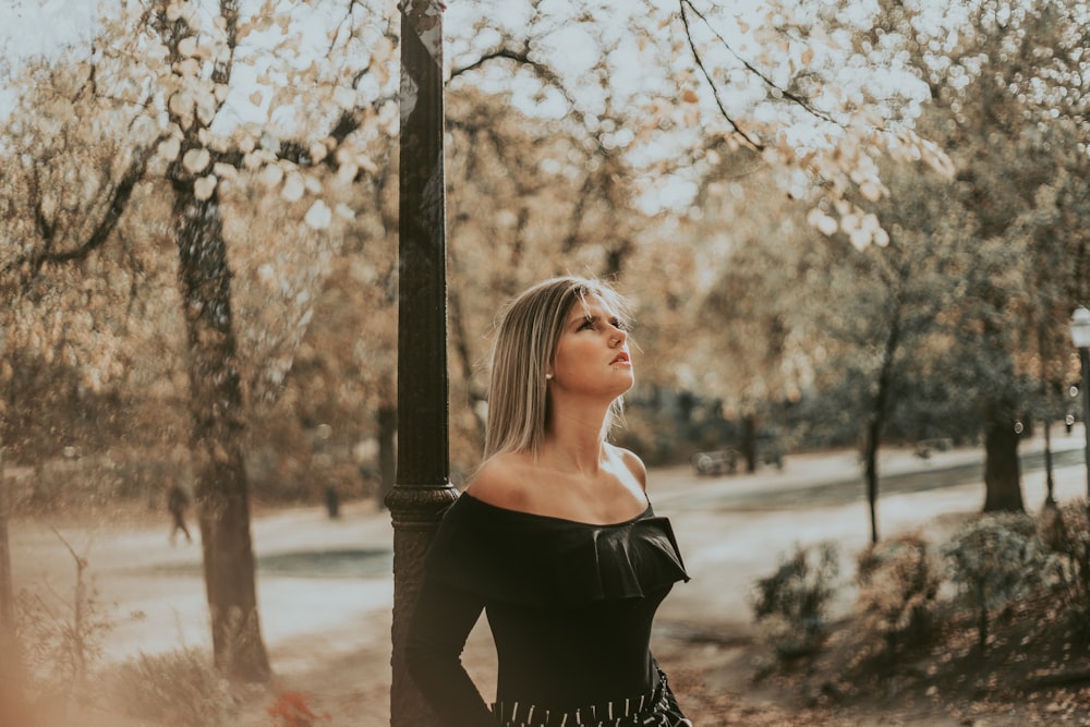 mulher no vestido preto do ombro fora de pé perto da árvore