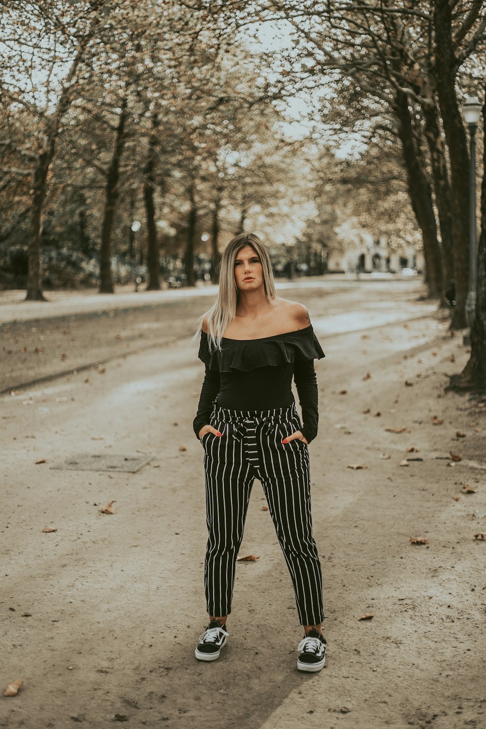 woman in black off-shoulder blouse with hands on pocket while standing near trees