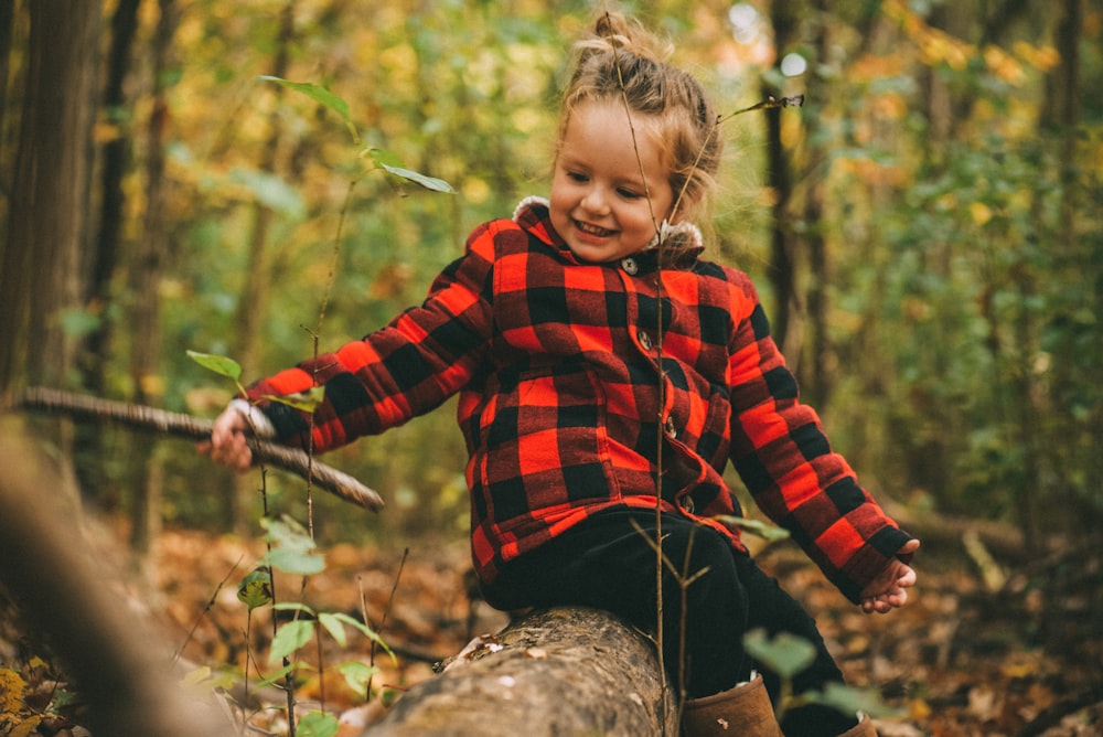 girl in red and black jacket sitting on brown log outdoors