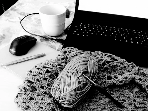 A cozy workspace with yarn, crochet hooks, and a laptop showing a digital pattern download page.