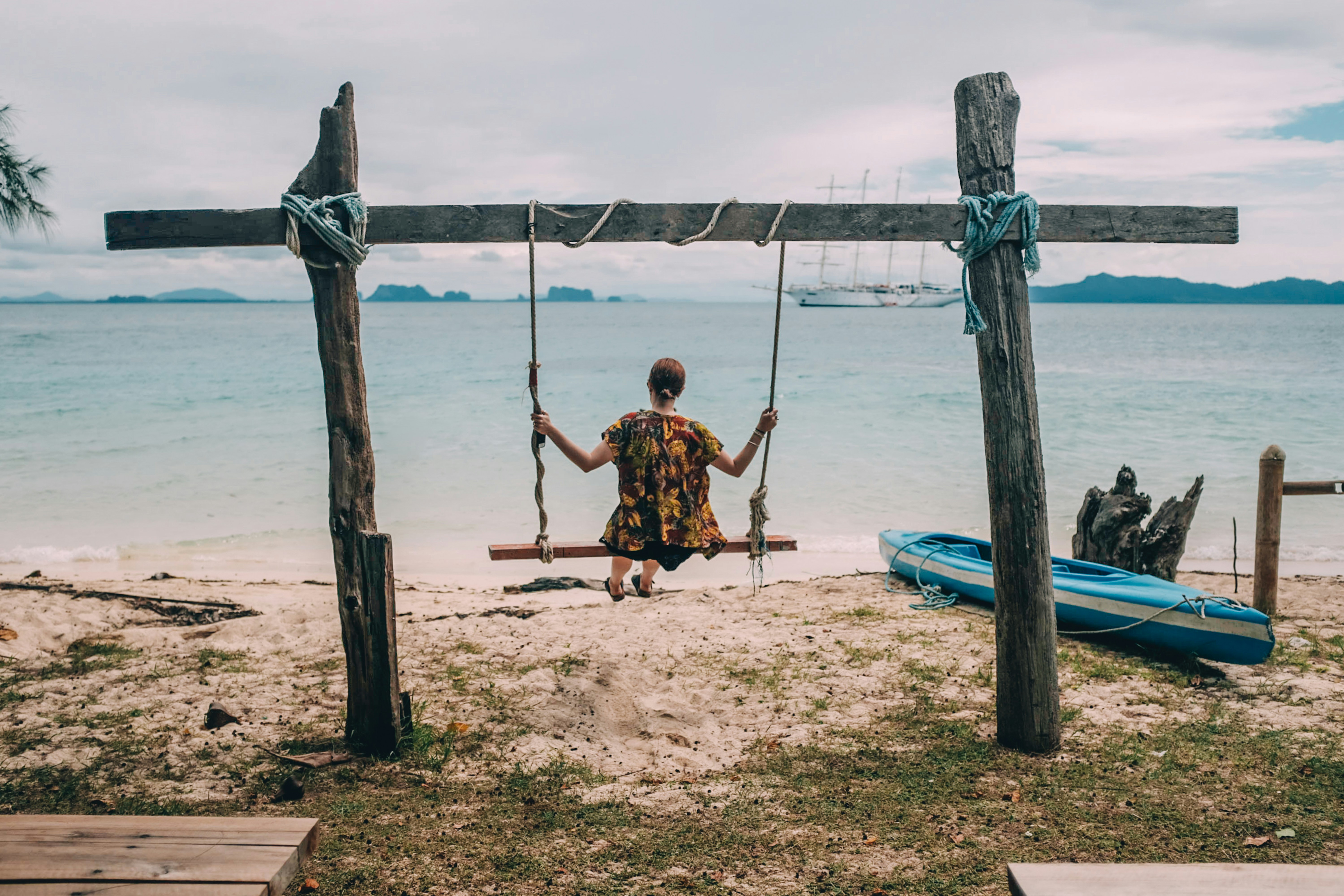 woman sitting on swing facing the ocean during day
