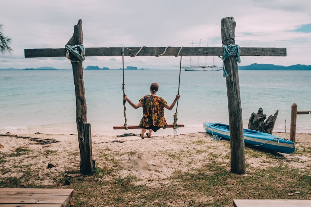 woman sitting on swing facing the ocean during day