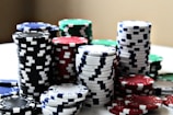 Stacks of colorful poker chips are arranged in piles on a white surface. The chips are blue, red, green, black, and white, each color having distinct markings.