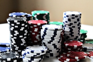 Stacks of colorful poker chips are arranged in piles on a white surface. The chips are blue, red, green, black, and white, each color having distinct markings.
