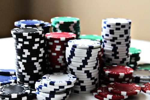 Stacks of colorful poker chips are arranged in piles on a white surface. The chips are blue, red, green, black, and white, each color having distinct markings.