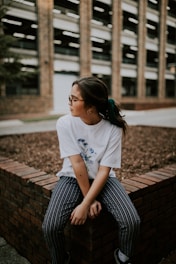 shallow focus photo of woman in white crew-neck T-shirt sitting on concrete bench