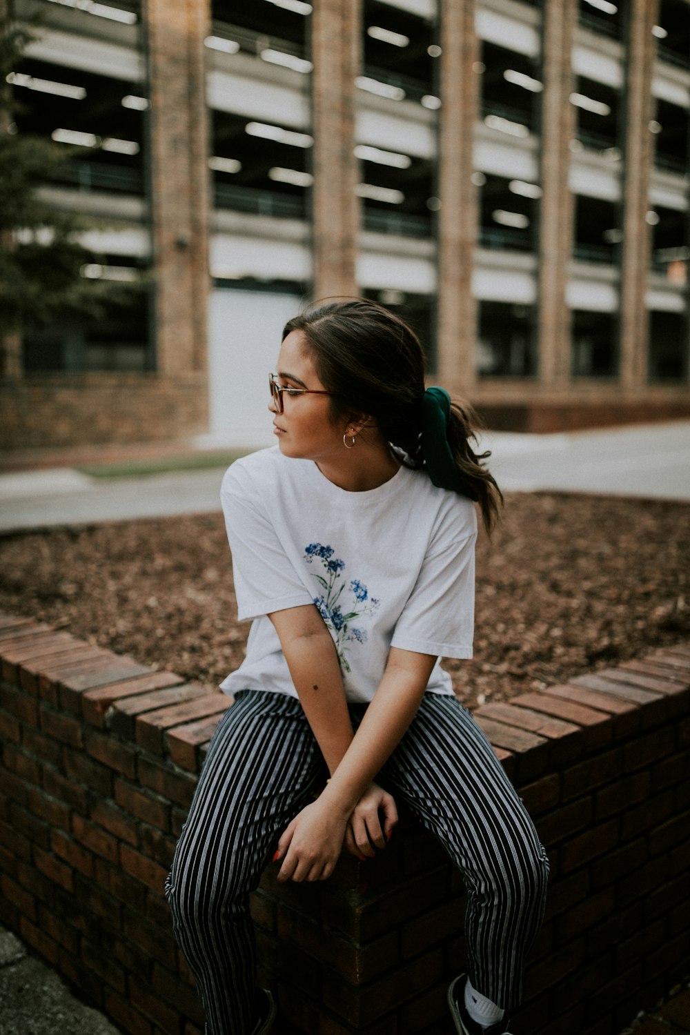 flaches Foto einer Frau im weißen T-Shirt mit Rundhalsausschnitt, die auf einer Betonbank sitzt