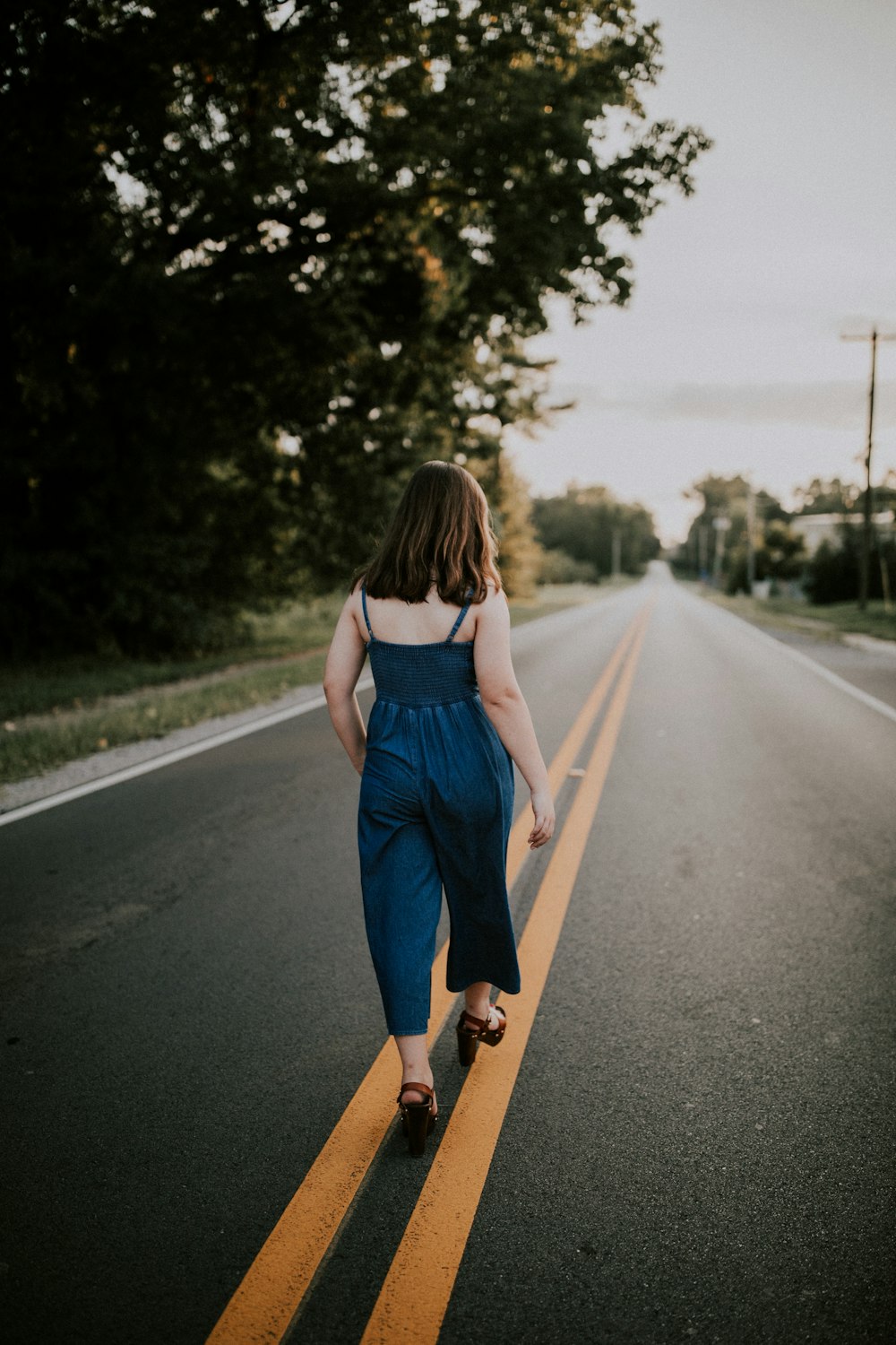 woman walking in the middle of black asphalt road during daytime