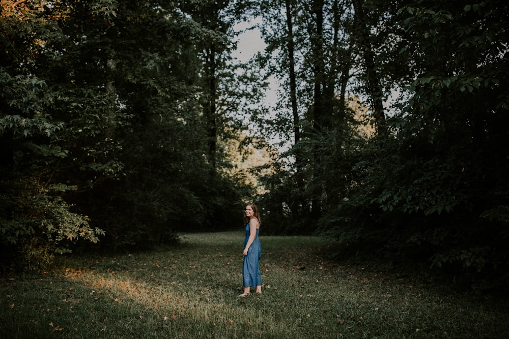 woman standing on grass field between trees