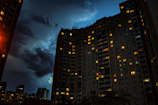 Evening shot of a completed apartment tower illuminated with warm lights against a clear sky.