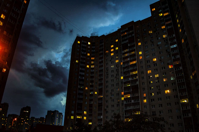 Evening shot of a completed apartment tower illuminated with warm lights against a clear sky.