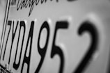 Close-up of a California license plate showing black characters including the letters and numbers 7YDA952 in a monochromatic color scheme.