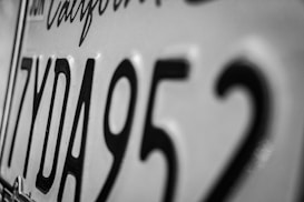 Close-up of a California license plate showing black characters including the letters and numbers 7YDA952 in a monochromatic color scheme.