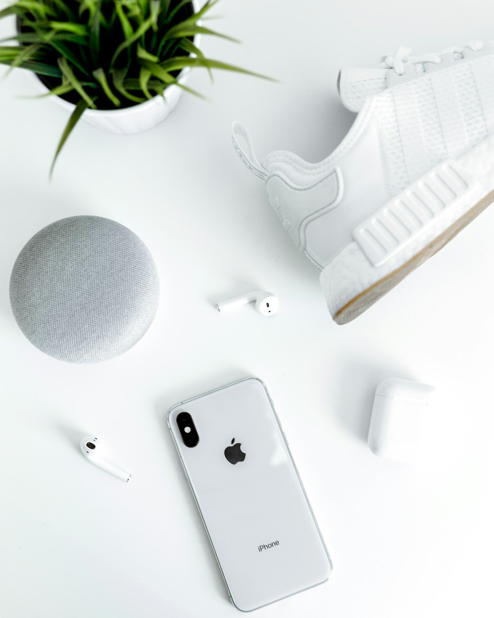 흰색 아디다스 NMD 신발에 가까운 은색 iPhone X, 케이스가 있는 AirPods, 분필 Google Home Mini