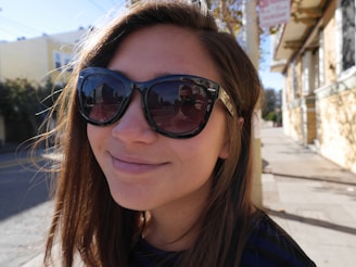 A smiling person wearing trendy sunglasses outdoors on a sunny day.