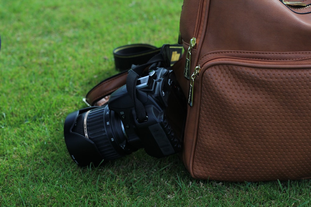 cámara de video al lado de una mochila marrón sobre hierba verde