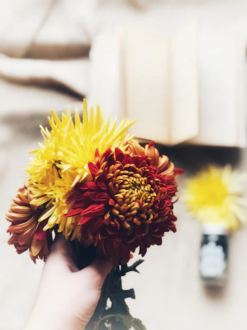 A hand holding a small bouquet of freshly picked wildflowers with the book resting nearby.