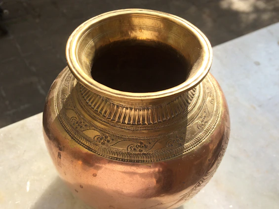 A close-up of a polished brass pot with intricate Indian engravings, resting on a wooden kitchen counter.