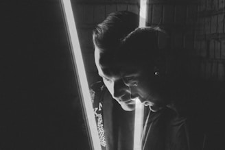 A grayscale portrait features a double exposure effect, capturing two profiles of a person facing opposite directions. A bright vertical light bisects the image, adding dramatic contrast.