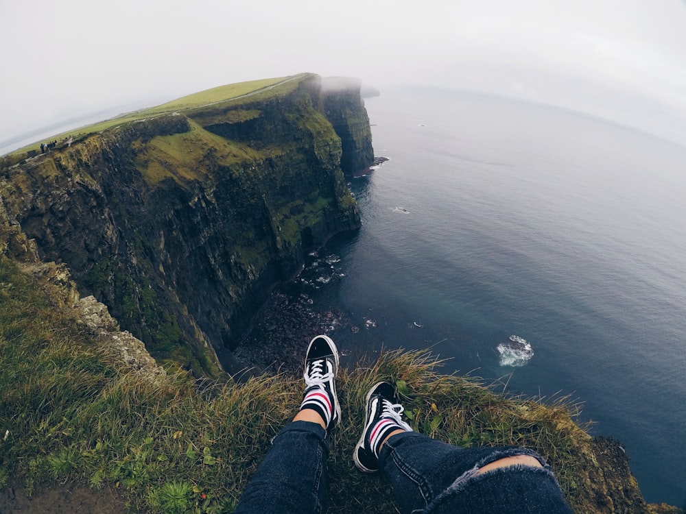 person sitting on cliff under white sky