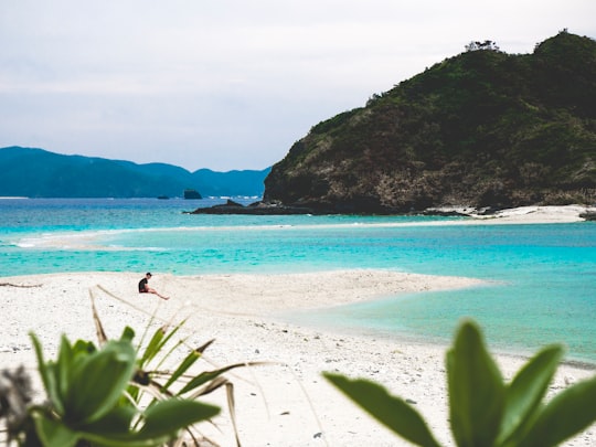 person sitting on seashore facing blue ocean in Zamami Island Japan