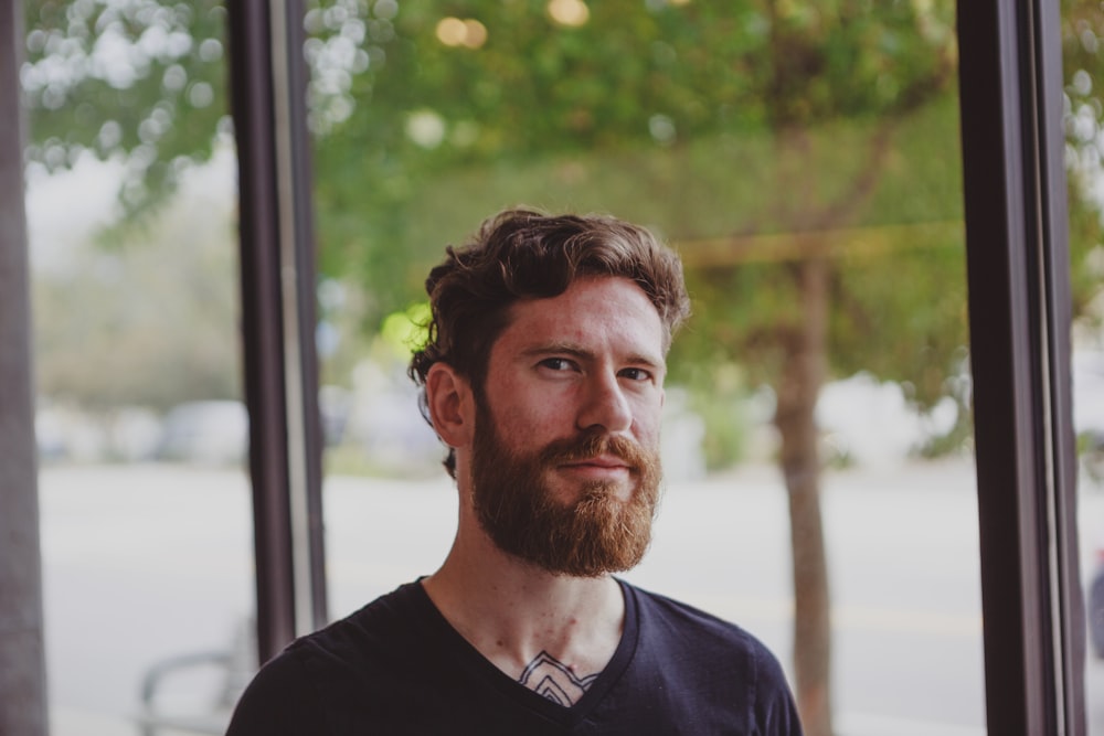 selective focus photo of smiling man standing beside window