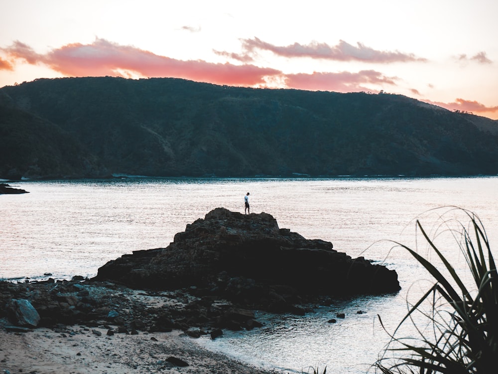 person standing on rock formation near body of water