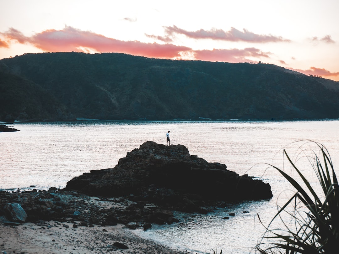 person standing on rock formation near body of water,