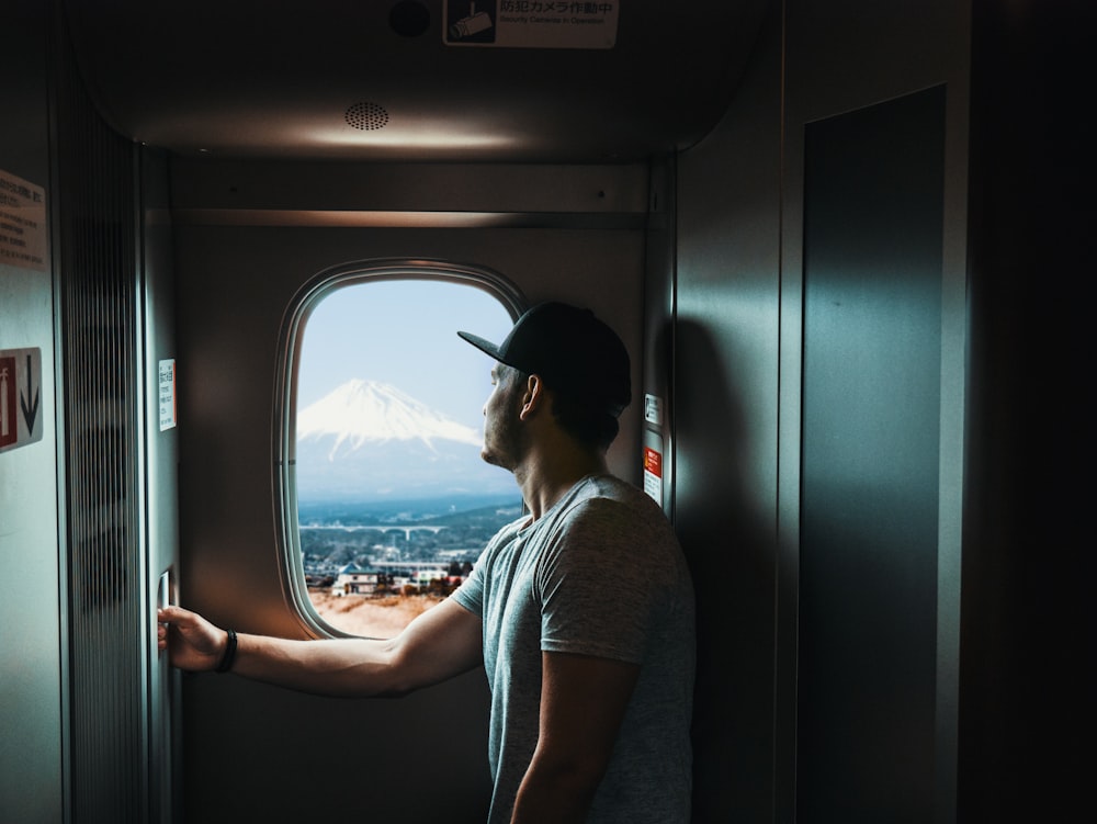 man standing near window overlooking snow capped mountain