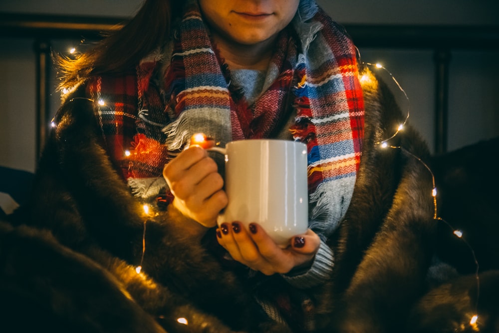 foto de foco raso de pessoa usando caneca de cerâmica branca