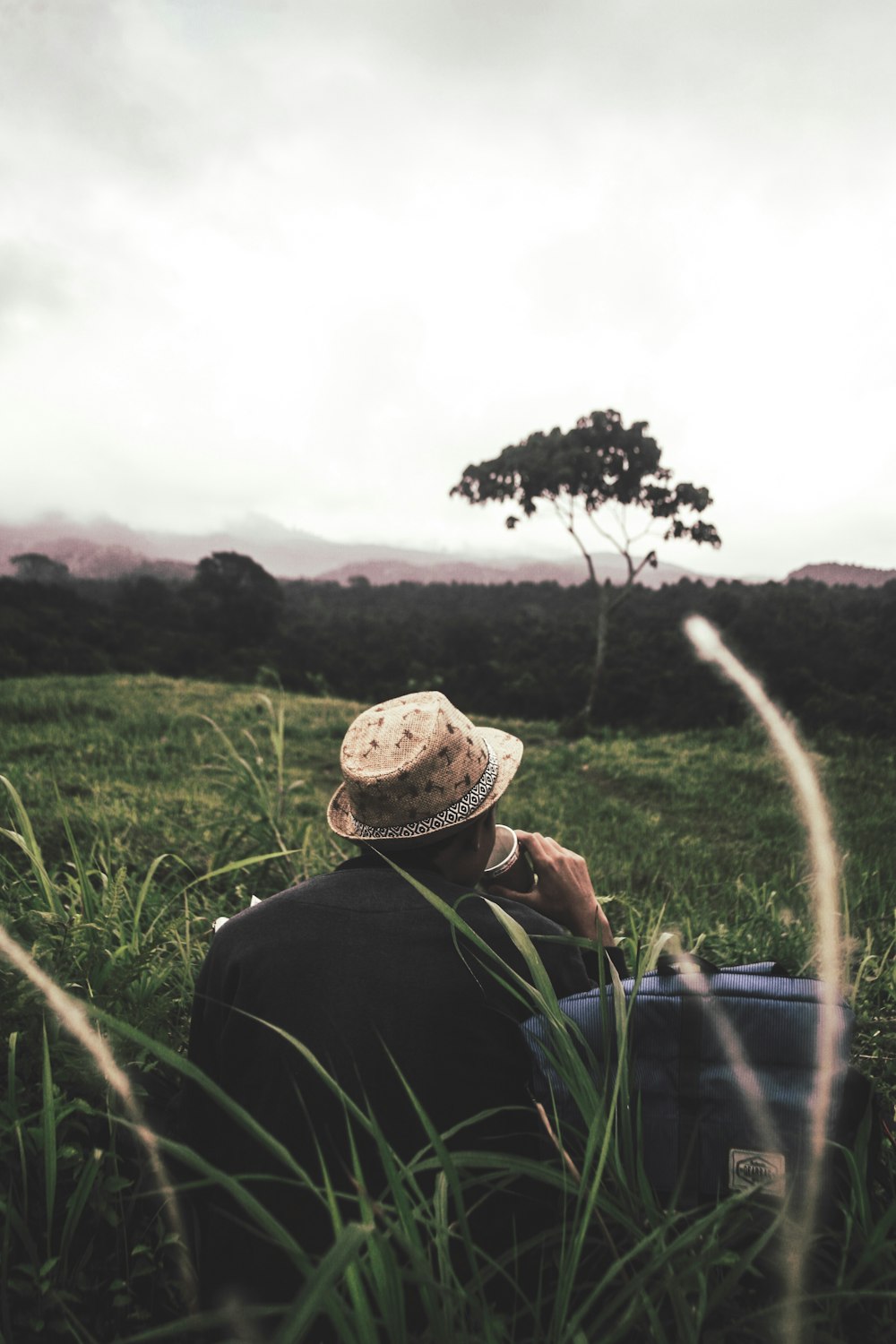 man sitting on green grass beside bag under nimbus clouds