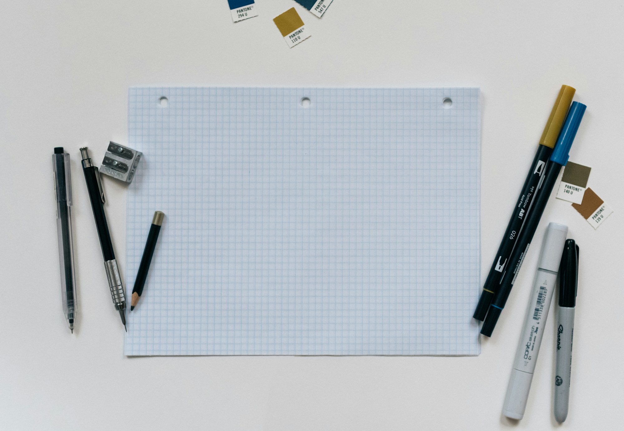 A blank piece of graph paper with a variety of pens to either side.