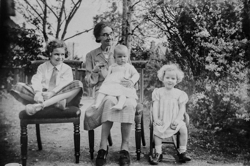 Mujer sosteniendo niño pequeño con dos niños al lado sentado en la silla foto en escala de grises