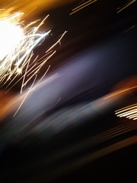 A dynamic display of bright, white and yellow sparks streak across a dark background, creating an abstract and energetic visual. The blurred movement suggests motion and spontaneity.