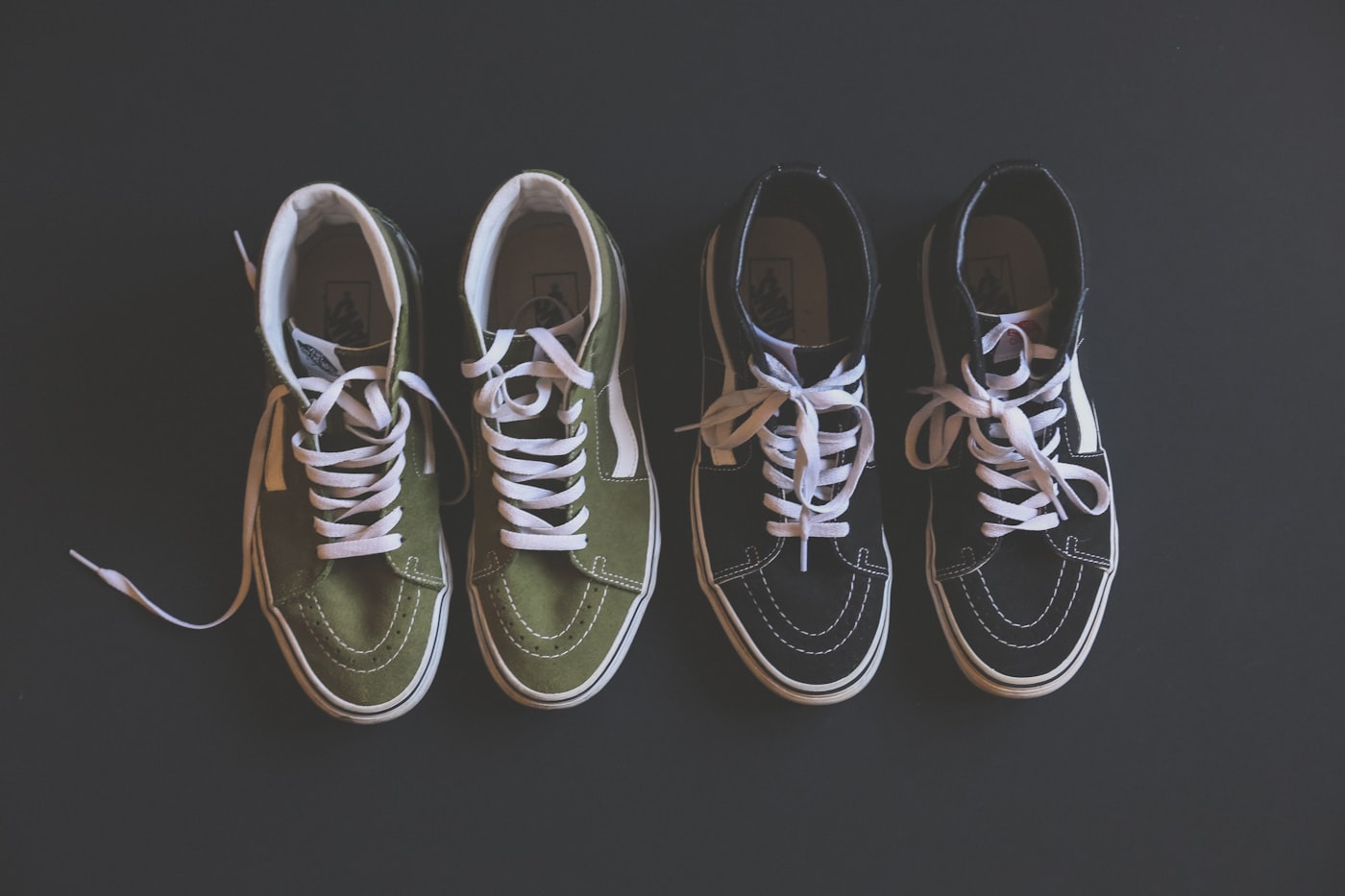 Two pairs of Vans Sk8-Hi high-top sneakers arranged on a dark surface