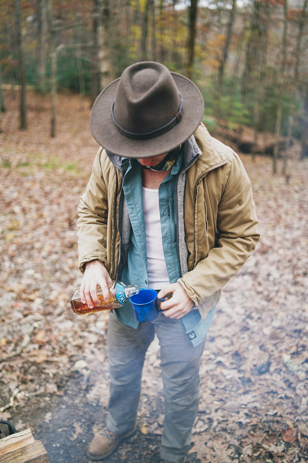 homme portant un chapeau brun versant du liquide sur la tasse bleue