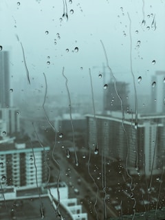 a rain-covered window blurs the buildings in the city, evoking feelings of weariness