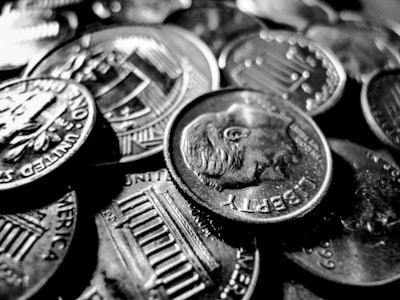 A close-up view of multiple coins, primarily featuring dimes. The coins are piled together, emphasizing the intricate designs and text such as 'Liberty' and 'United States of America.' The image is rendered in black and white, highlighting the reflective surfaces of the coins.
