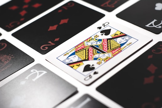 A close-up view of playing cards laid out in a grid pattern, with a prominent Queen of Spades card in the center. The other cards include assorted numbers and suits, all arranged neatly.
