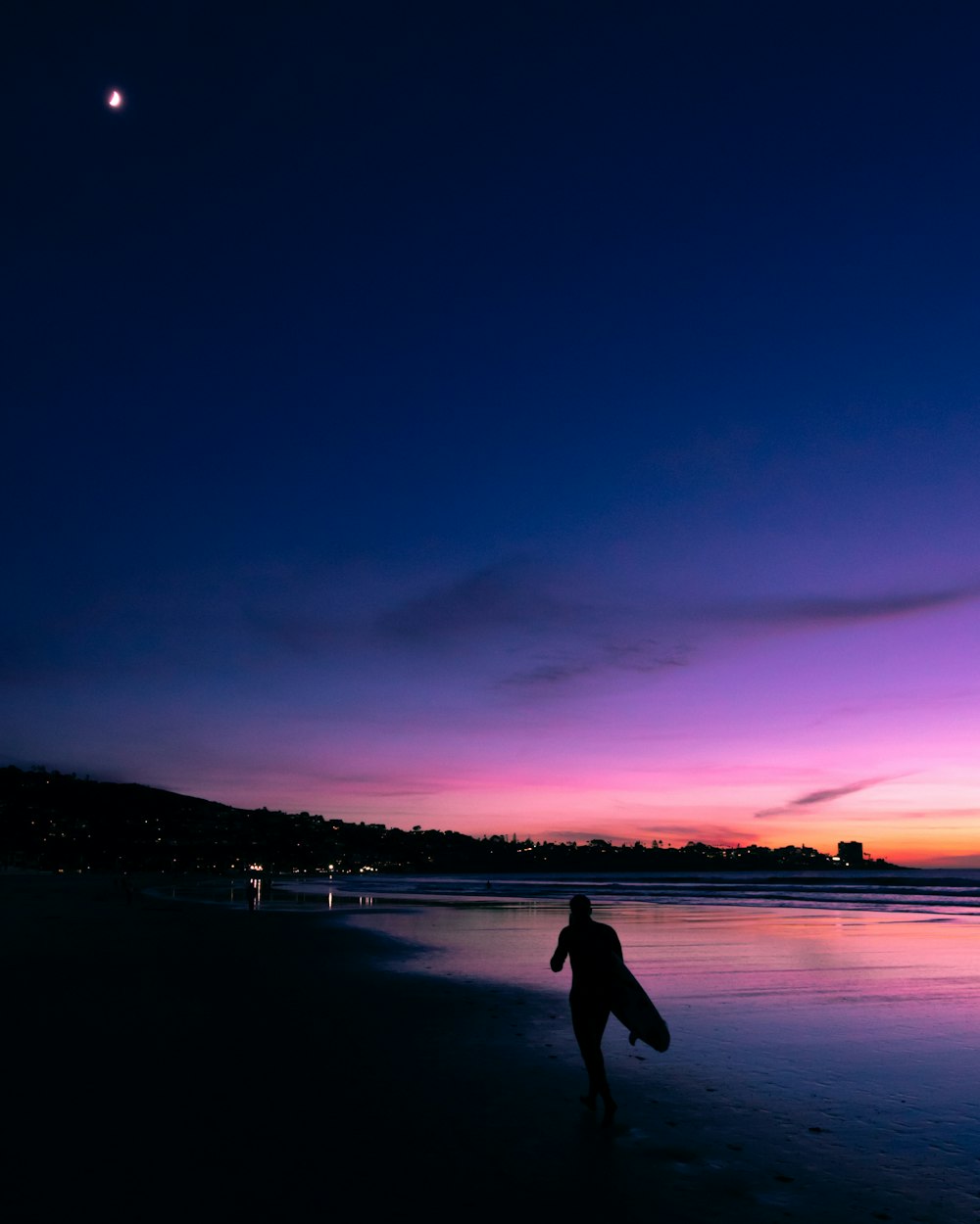 silhouette of person carrrying surfboard while walking on seashore