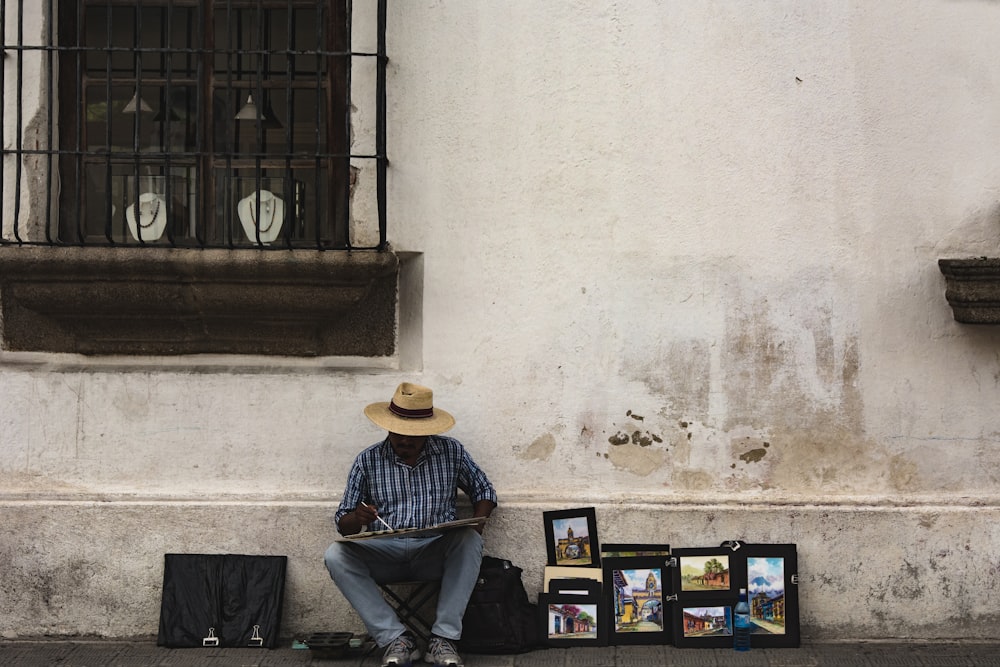 man in blue white shirt sitting near the wall painting on canvas