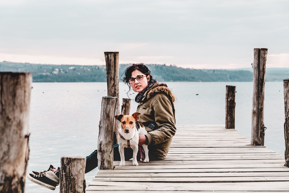 Mujer sentada en muelle de madera marrón con perro