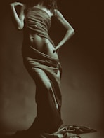 An intimate photo of a woman silhouetted against a dark backdrop, emphasizing the graceful lines of her body.