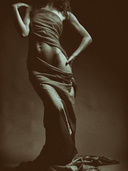 An intimate photo of a woman silhouetted against a dark backdrop, emphasizing the graceful lines of her body.