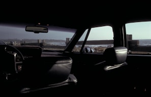 Close-up of a car interior with sand-colored leather seats and a view of the sea through the windshield.