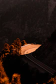 A winding mountain road bathed in golden sunset light with a motorcycle parked at the edge.